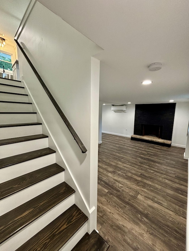 stairway featuring wood-type flooring, an AC wall unit, and a brick fireplace