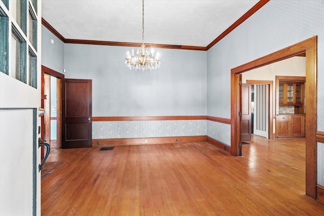 unfurnished room featuring hardwood / wood-style flooring, a notable chandelier, and crown molding