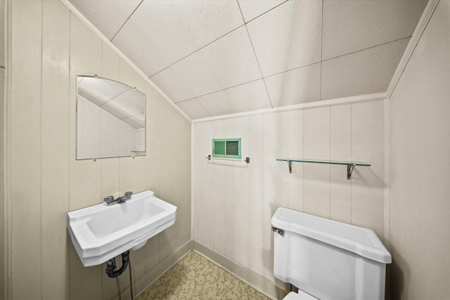 bathroom featuring wood walls, sink, vaulted ceiling, and toilet