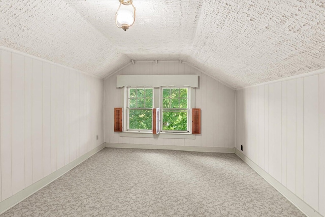 additional living space with carpet flooring, a textured ceiling, wooden walls, and vaulted ceiling