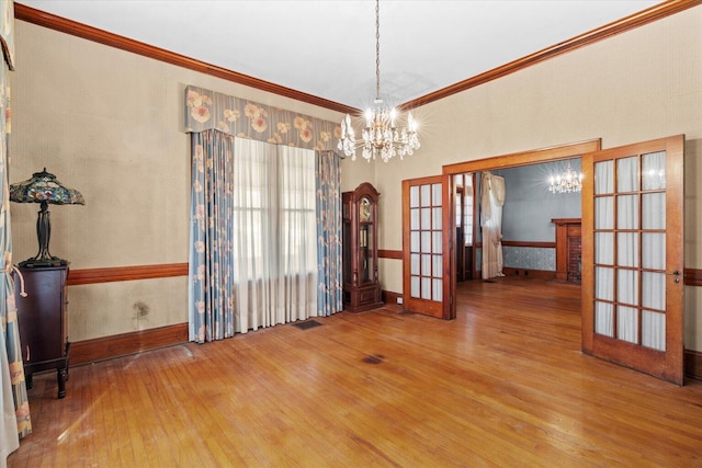 unfurnished dining area with french doors, hardwood / wood-style floors, a notable chandelier, and ornamental molding