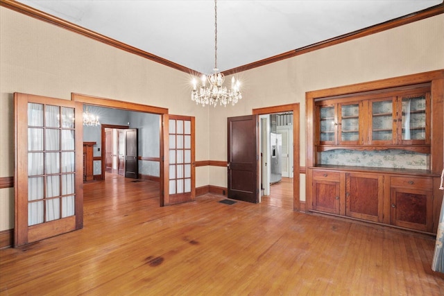 unfurnished dining area featuring a chandelier, french doors, ornamental molding, and light hardwood / wood-style flooring