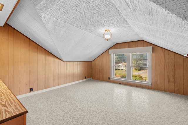 additional living space featuring wood walls, lofted ceiling, and a textured ceiling