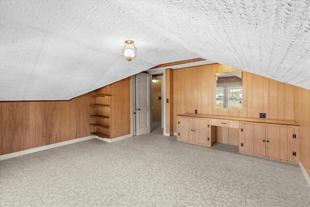 bonus room with a textured ceiling, wooden walls, and lofted ceiling