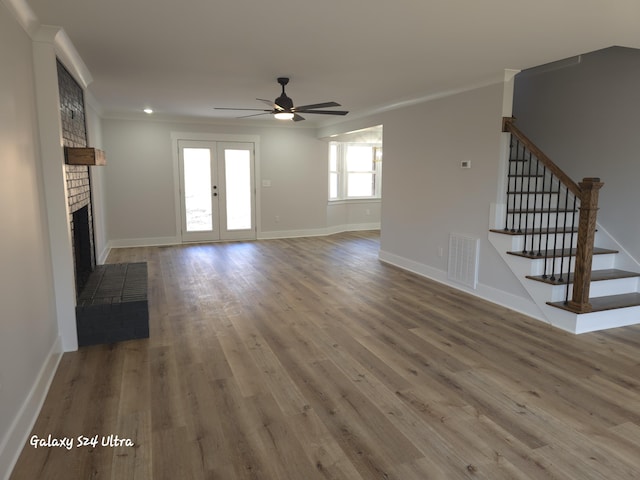 unfurnished living room featuring wood-type flooring, ceiling fan, crown molding, a brick fireplace, and french doors