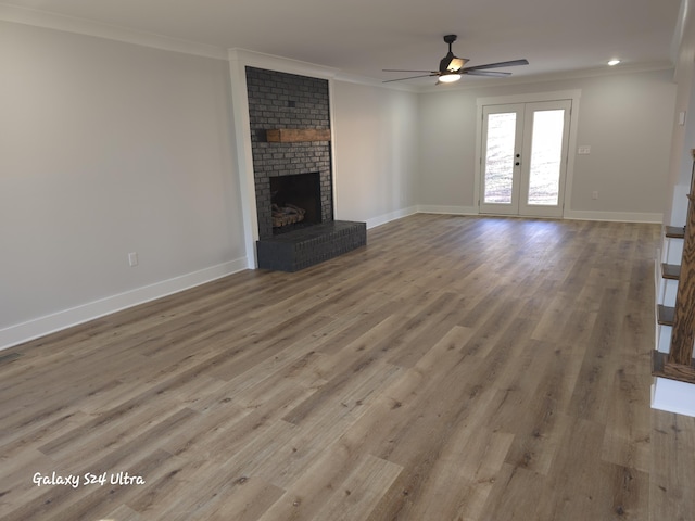 unfurnished living room featuring ornamental molding, a brick fireplace, light hardwood / wood-style flooring, and french doors