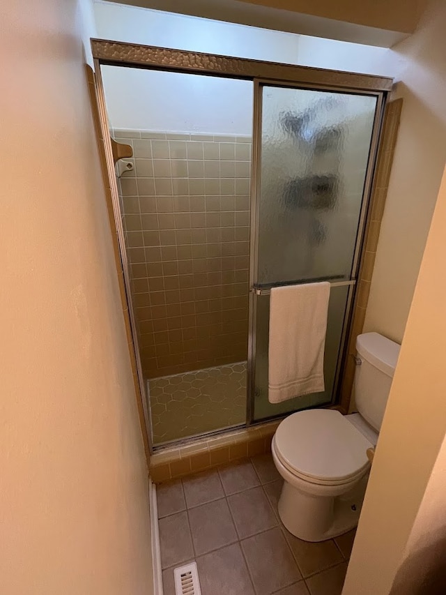 bathroom featuring tile patterned floors, toilet, and a shower with door