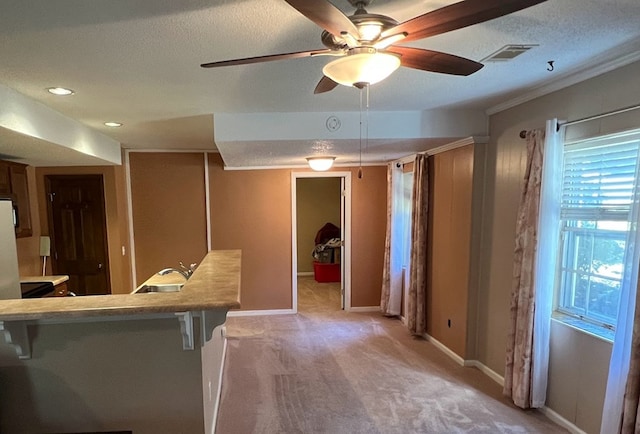 interior space with ceiling fan, kitchen peninsula, light colored carpet, a textured ceiling, and a breakfast bar area