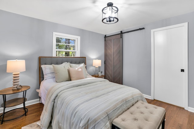 bedroom featuring a barn door, wood-type flooring, and a notable chandelier