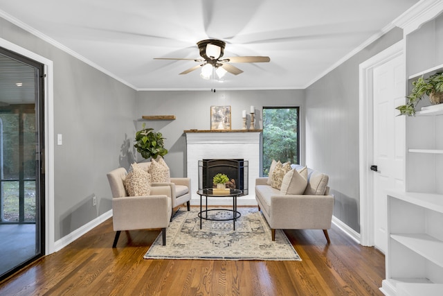 living room featuring built in shelves, ceiling fan, dark hardwood / wood-style flooring, crown molding, and a fireplace