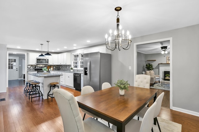 dining area with hardwood / wood-style floors, ceiling fan with notable chandelier, and a brick fireplace