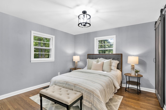 bedroom featuring dark hardwood / wood-style floors, a barn door, and a chandelier