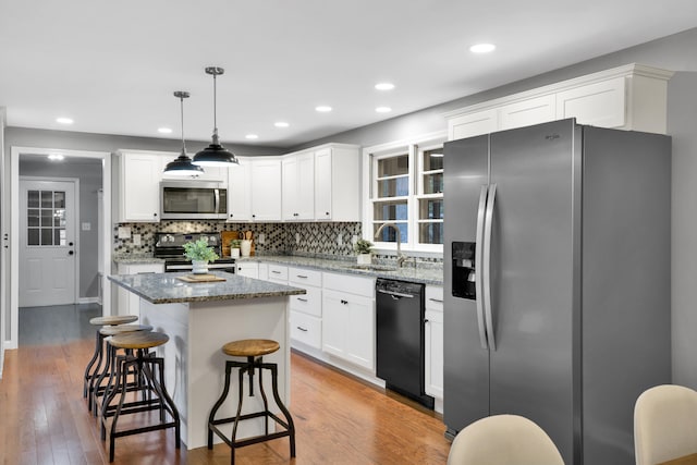 kitchen with black appliances, white cabinets, hanging light fixtures, hardwood / wood-style flooring, and a kitchen island