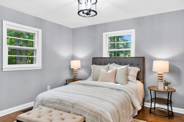 bedroom featuring an inviting chandelier, multiple windows, and dark wood-type flooring