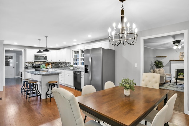 dining space featuring wood-type flooring, ceiling fan with notable chandelier, and sink