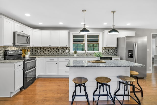 kitchen featuring pendant lighting, white cabinets, light wood-type flooring, light stone counters, and stainless steel appliances