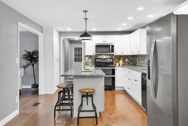 kitchen with light wood-type flooring, light stone counters, stainless steel appliances, pendant lighting, and a kitchen island