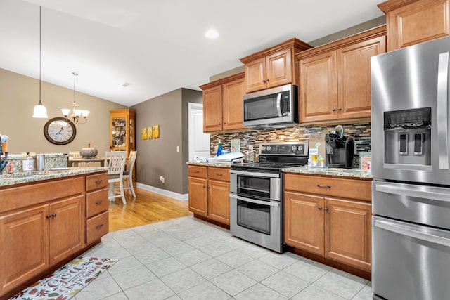 kitchen featuring lofted ceiling, an inviting chandelier, light tile patterned floors, light stone counters, and stainless steel appliances