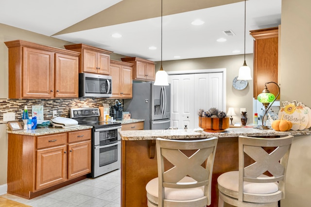 kitchen with light stone counters, pendant lighting, and stainless steel appliances