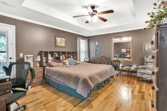 bedroom with light hardwood / wood-style floors, multiple windows, a tray ceiling, and ceiling fan