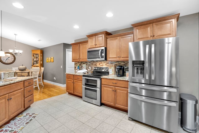 kitchen with light stone countertops, stainless steel appliances, vaulted ceiling, light tile patterned floors, and a notable chandelier