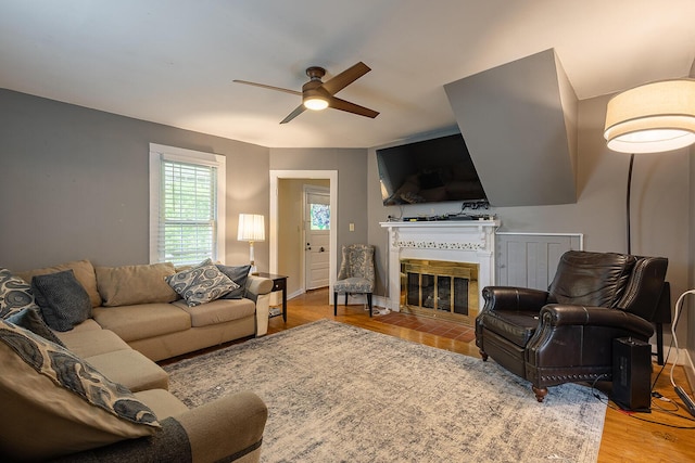 living room with a ceiling fan, a fireplace with flush hearth, and wood finished floors