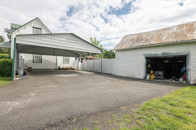 view of home's exterior featuring metal roof, asphalt driveway, a standing seam roof, fence, and a carport
