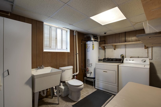 laundry area with gas water heater, light tile patterned flooring, a sink, wooden walls, and independent washer and dryer