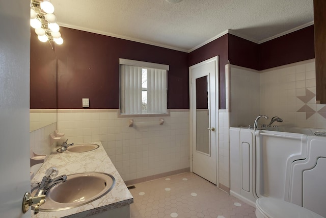 full bath with double vanity, a garden tub, a textured ceiling, and a sink