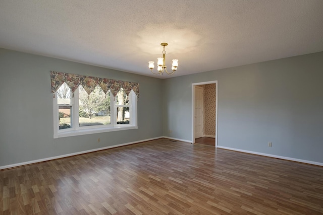 empty room with a chandelier, a textured ceiling, baseboards, and wood finished floors