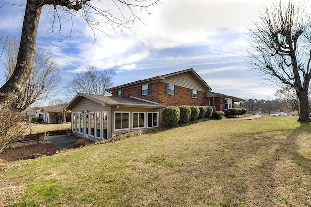 rear view of house featuring a sunroom, a yard, and brick siding