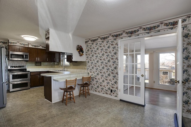 kitchen with a breakfast bar area, stainless steel appliances, light countertops, dark brown cabinetry, and a peninsula