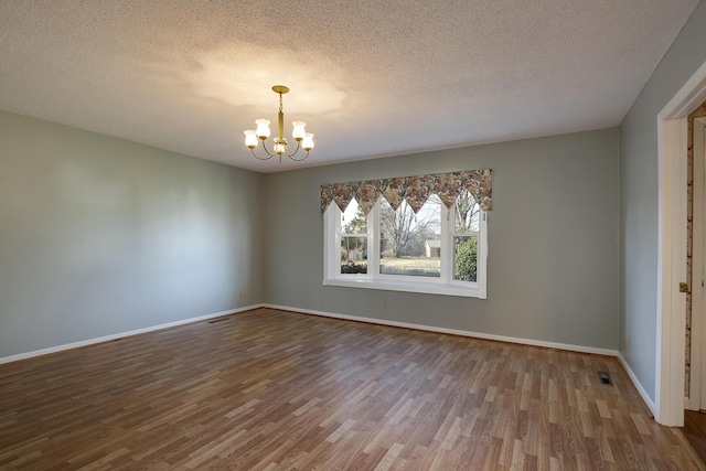 unfurnished room featuring a notable chandelier, a textured ceiling, baseboards, and wood finished floors