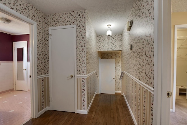 hall featuring hardwood / wood-style flooring, a wainscoted wall, a textured ceiling, and wallpapered walls