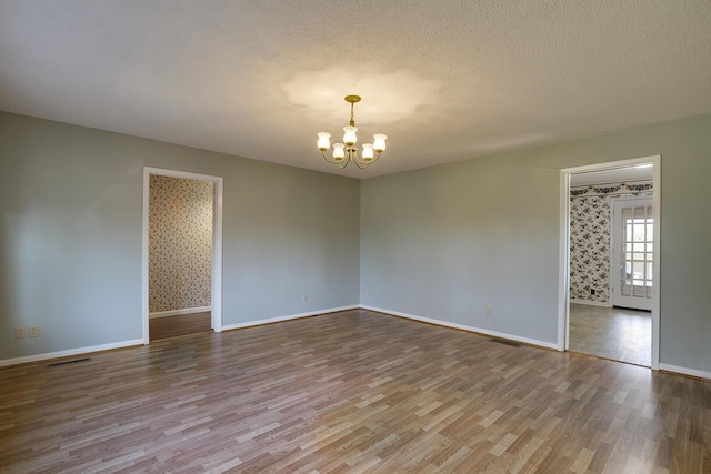 empty room featuring baseboards, visible vents, wood finished floors, a textured ceiling, and a chandelier