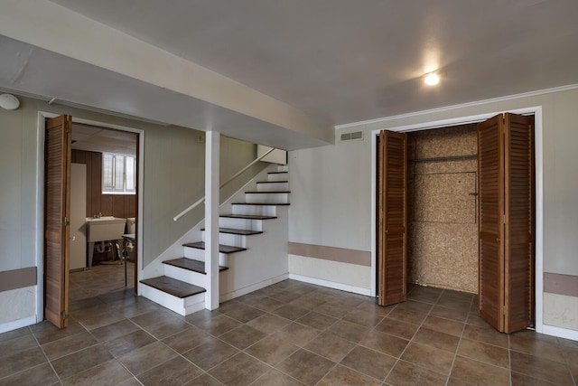 interior space featuring visible vents, baseboards, stairway, wood walls, and dark tile patterned floors