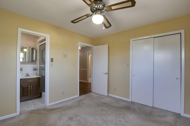 unfurnished bedroom featuring carpet floors, a closet, connected bathroom, a sink, and baseboards