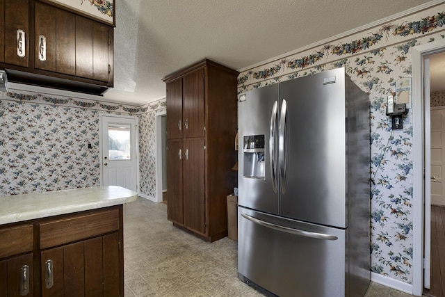 kitchen with a textured ceiling, baseboards, light countertops, stainless steel fridge with ice dispenser, and wallpapered walls