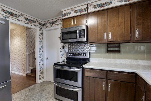 kitchen with light countertops, decorative backsplash, appliances with stainless steel finishes, a textured ceiling, and wallpapered walls