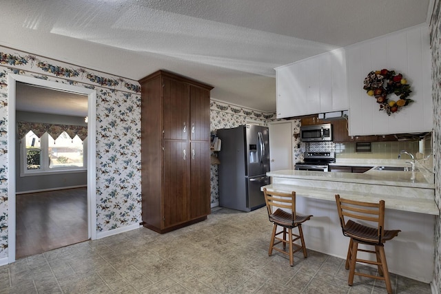 kitchen featuring stainless steel appliances, light countertops, a sink, a peninsula, and wallpapered walls