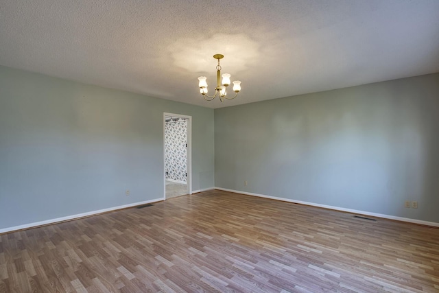 empty room with a textured ceiling, visible vents, a notable chandelier, and wood finished floors