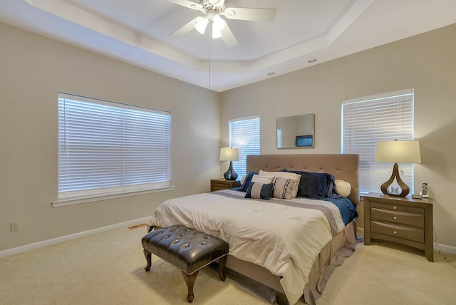 bedroom with light carpet, baseboards, a tray ceiling, and a ceiling fan