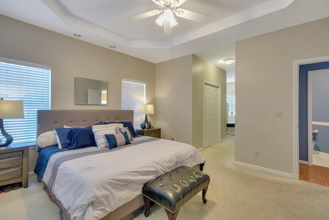 bedroom featuring light carpet, baseboards, a raised ceiling, a ceiling fan, and a closet