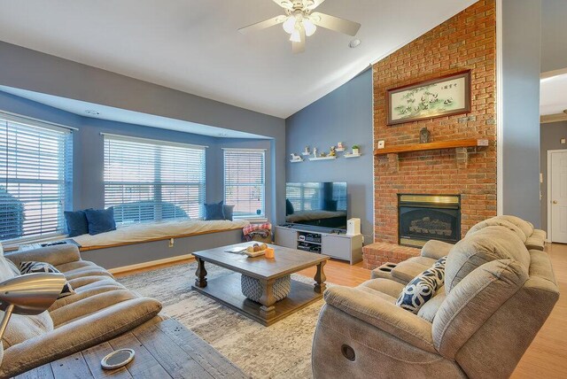 living room with ceiling fan, high vaulted ceiling, light wood-type flooring, and a brick fireplace