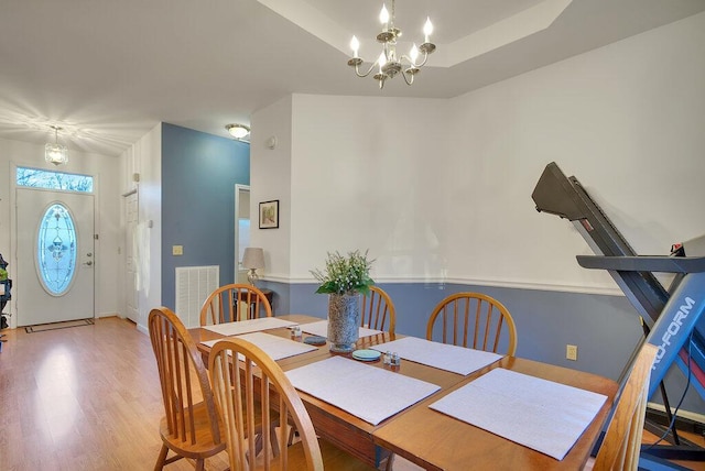 dining room featuring a notable chandelier, wood finished floors, visible vents, baseboards, and a tray ceiling