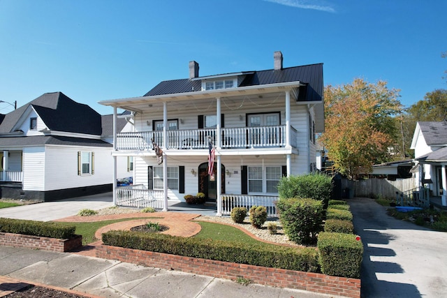 view of front of home featuring metal roof, a porch, a balcony, a standing seam roof, and a chimney