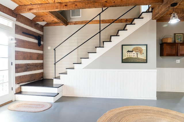 stairway with beam ceiling, wood walls, and concrete floors