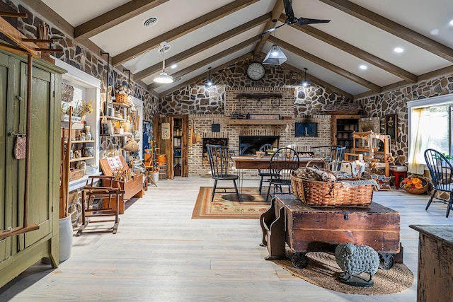 living room featuring ceiling fan, vaulted ceiling with beams, light wood-type flooring, and a brick fireplace