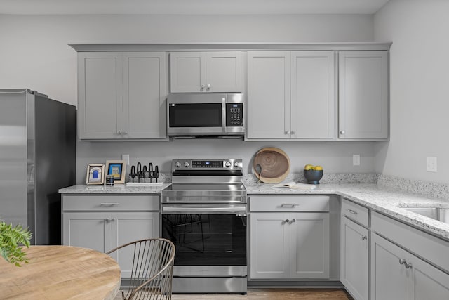 kitchen featuring gray cabinetry, light stone counters, stainless steel appliances, and hardwood / wood-style flooring