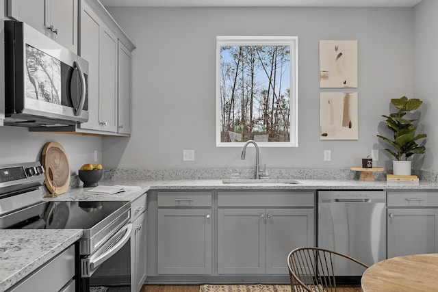 kitchen with gray cabinetry, sink, light stone countertops, and stainless steel appliances